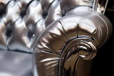 Zbliżenie na srebrną, pikowaną sofę z ozdobnie wygiętym, błyszczącym podłokietnikiem.