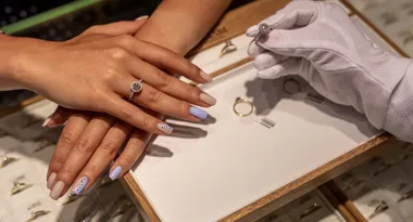 Dłoń z manicurem i pierścionkiem, obok w białej rękawiczce pokazuje kolejny pierścionek.